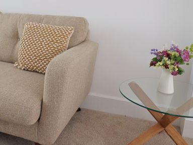 A beige sofa with a textured cushion next to a glass table with a vase of flowers at 47 Church Street in Lyme Regis