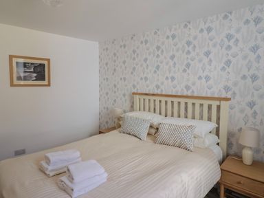 A bedroom with a bed with pillows and folded towels bedside tables with lamps and framed picture on the wall at 47 Church Street in Lyme Regis