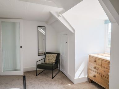 A room with a green armchair with a cushion a wooden chest of drawers a full length mirror and a door at 47 Church Street in Lyme Regis