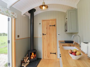 A kitchen with a wood burning stove next to a wooden door and a countertop with a sink and bowl of apples at Goose Whistle Hut in Foxham
