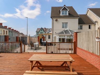 A backyard with wooden deck and picnic table and a patio with table and chairs behind a house at Alban Road in Llanelli