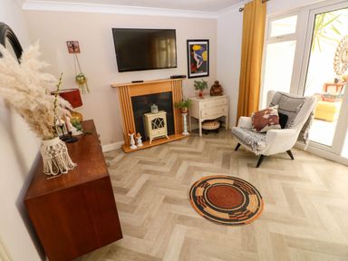 A living room with a TV above a fireplace an armchair and a round rug at Alban Road in Llanelli