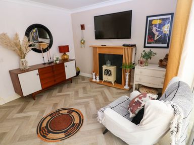 A living room with a wall-mounted tv above a fireplace and a sideboard with decorations at Alban Road Llanelli