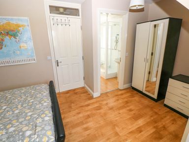 A bedroom with a bed, wardrobe with mirror, chest of drawers, door, and an entrance to a bathroom at Alban Road in Llanelli