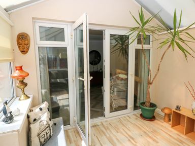 A conservatory room with glass doors, a potted plant, cushions on a bench, and decorative items at Alban Road in Llanelli