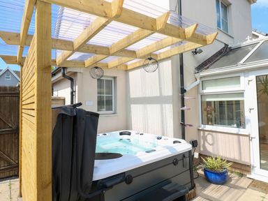 An outdoor hot tub under a wooden pergola attached to a house with a blue potted plant on the ground at Alban Road in Llanelli