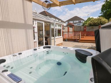 An outdoor hot tub next to a conservatory in a backyard with a wooden deck and fence at Alban Road in Llanelli