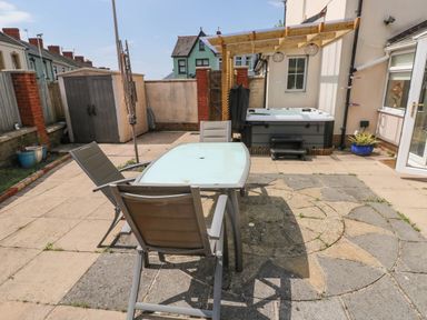 A backyard patio with a table and three chairs a hot tub under a wooden pergola and a storage shed at Alban Road in Llanelli