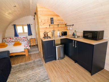 A small room with a bed with floral bedding a kitchenette with black cabinets a microwave a sink and a stove at Holbein in Matlock