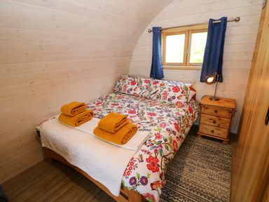 A bedroom with a floral bedspread bed two yellow towels on it a wooden nightstand with a lamp and a window with blue curtains at Holbein in Matlock