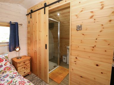 A bedroom with floral bedding beside a wooden nightstand and lamp next to a sliding wooden door leading to a shower area at Holbein in Matlock