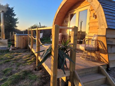 A wooden cabin with a small deck with two chairs and a hot tub outside surrounded by grass at Holbein in Matlock