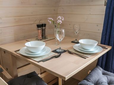 A dining table set with two place settings including bowls plates cutlery and wine glasses with a salt and pepper shaker and flowers in a glass vase at Holbein Matlock