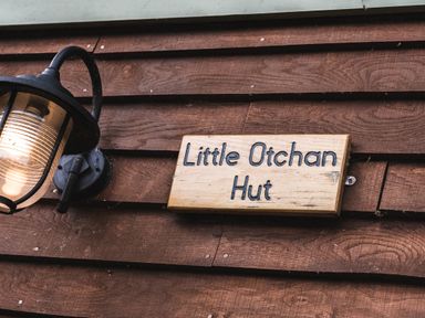 A wooden sign that says Little Otchan Hut next to a wall-mounted lantern on a wooden wall at Little Otchan Shepherd's Hut in Halsham near Roos