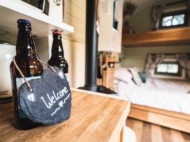 A wooden countertop with two bottles and a heart shaped welcome sign in a small cabin bedroom at Little Otchan Shepherd's Hut Halsham near Roos