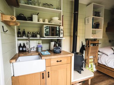A small kitchen area with a sink microwave open shelves and a stove next to a bed at Little Otchan Shepherd's Hut in Halsham near Roos
