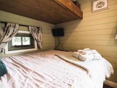 A bedroom with a bed near a small window with curtains and a television mounted on the wall at Little Otchan Shepherd's Hut Halsham near Roos