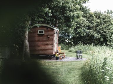 A wooden shepherd's hut with a small window and a chair outside on grass surrounded by trees at Little Otchan Shepherd's Hut Halsham near Roos