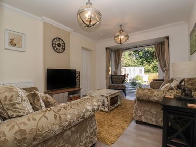 A living room with patterned sofas a rug a wooden coffee table a television on a stand and an open door leading to a garden at The Corner House in Ufford near Woodbridge