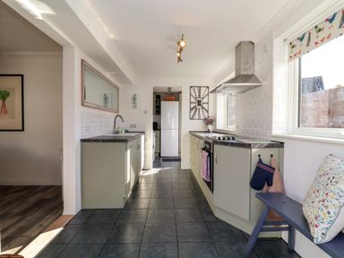 A kitchen with a tiled floor cabinets a stove a sink a refrigerator a bench with cushions and windows at The Corner House in Ufford near Woodbridge