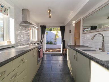 A kitchen with a stove oven and sink with a faucet and open doors to a garden at The Corner House in Ufford near Woodbridge