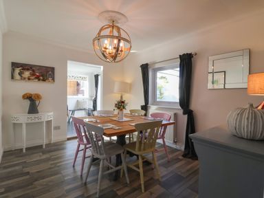 A dining room with a wooden table surrounded by six chairs and a chandelier at The Corner House in Ufford near Woodbridge