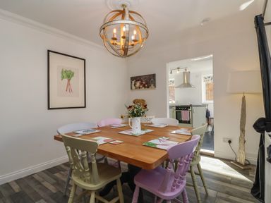A dining room with a wooden table and mixed colored chairs and a kitchen visible through an open doorway at The Corner House in Ufford near Woodbridge