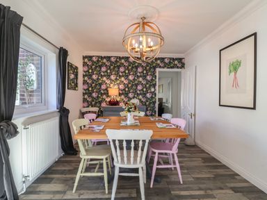 A dining room with a wooden table and pastel-colored chairs a floral wallpaper and a chandelier at The Corner House in Ufford near Woodbridge