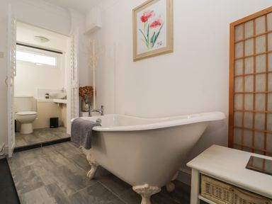 A bathroom with a clawfoot bathtub towel rack and a toilet in the background at The Corner House in Ufford near Woodbridge