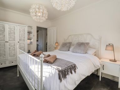 A bedroom with a white metal bed frame two fluffy pillows and a blanket on the bed a white nightstand with a lamp and a wardrobe with patterned doors at The Corner House in Ufford near Woodbridge