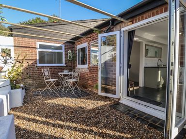 An outdoor patio with a white metal table and two chairs on stone tiles outside a brick building with open glass doors at The Corner House in Ufford near Woodbridge