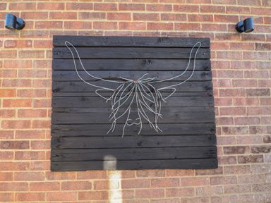 A brick wall with two black lights and a black wooden panel with wire art of a bull head at The Corner House in Ufford near Woodbridge