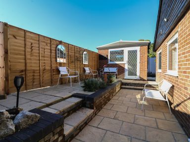 An outdoor patio area with white metal chairs a brick building with diamond patterned windows and wooden fencing at The Corner House in Ufford near Woodbridge