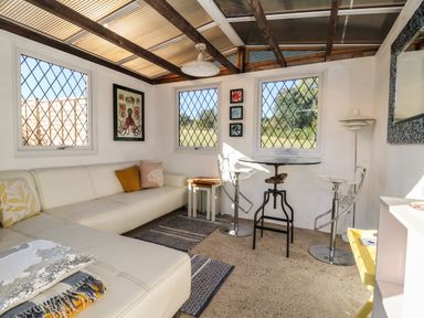 A sunroom with a white sectional sofa pillows and a small round table with two clear chairs at The Corner House in Ufford near Woodbridge
