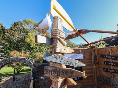 A wooden post with directional signs and a seagull decoration in a garden area at The Corner House in Ufford near Woodbridge