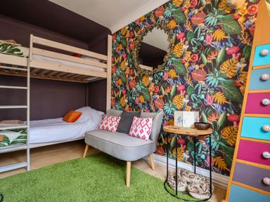 A bedroom with bunk beds a gray loveseat with pillows a round wooden side table and a colorful chest of drawers at The Corner House in Ufford near Woodbridge