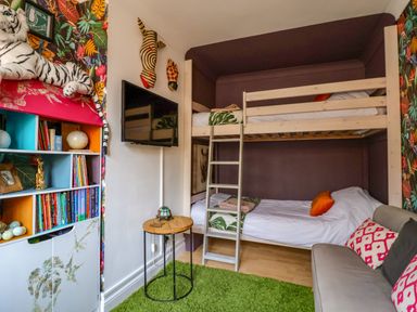 A bedroom with bunk beds a small sofa colorful bookshelf and mounted tv at The Corner House in Ufford near Woodbridge