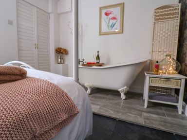 A bedroom with a bed with pink knit blanket and towels and a claw foot bathtub with a side table at The Corner House in Ufford near Woodbridge