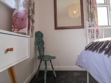 A bedroom corner with a green wooden chair white dresser floral curtains and a bed with a blanket at The Corner House in Ufford near Woodbridge