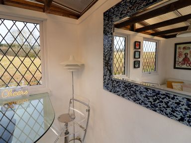 A small dining area with a glass table and transparent chair next to a window a floor lamp and a large mirror on the wall at The Corner House in Ufford near Woodbridge
