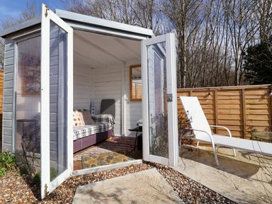 A garden shed with open glass doors next to a white lounge chair on a patio at The Corner House in Ufford near Woodbridge