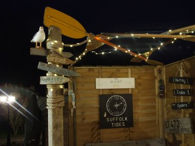A wooden post with directional signs and a fake seagull under string lights at night at The Corner House in Ufford near Woodbridge