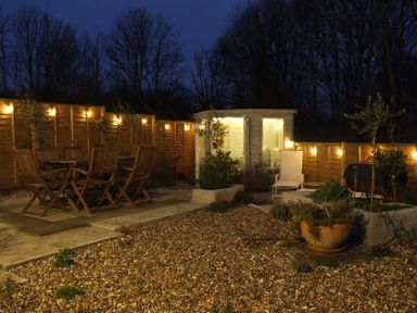 An outdoor garden area with wooden dining furniture a white chair plants and string lights on a wooden fence at The Corner House in Ufford near Woodbridge