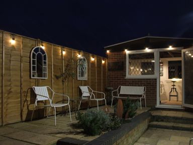 A patio with white metal chairs a small table and wall lights at The Corner House in Ufford near Woodbridge