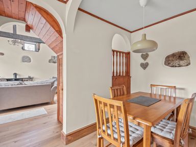 A dining area with a wooden table and four chairs next to an archway leading to a living room at The Dairy in St Neot