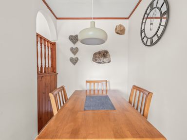 A dining room with a wooden table and chairs a hanging light a wall clock and heart decorations at The Dairy in St Neot
