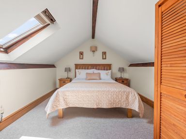 A bedroom with a double bed two bedside tables with lamps a skylight window and wooden beams at The Dairy in St Neot
