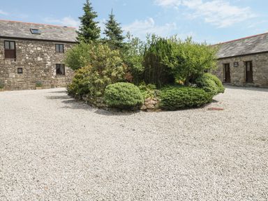 Gravel courtyard with stone buildings and a central garden of shrubs and trees at The Dairy in St Neot