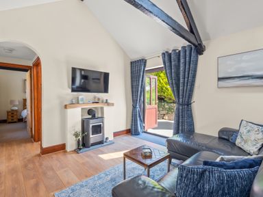 A living room with a leather sofa television and wood-burning stove at The Stables in St Neot