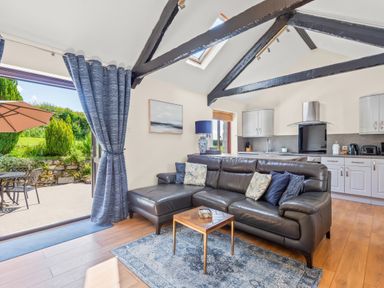 An open living room and kitchen with a leather sofa and small table near an open door to a patio at The Stables in St Neot